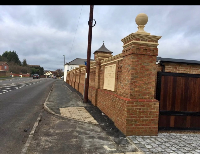 A high-end, decorative brick boundary wall featuring integrated pillars, intricate dentil brick coursing, and tiered stone pier caps topped with ornamental stone spheres.