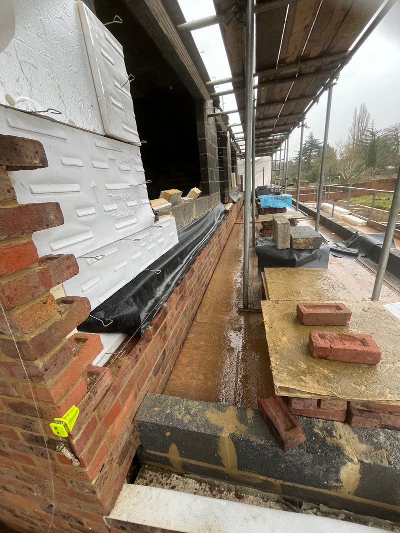 A professional masonry site showing the installation of high-grade cavity wall insulation between an external brick skin and internal blockwork.