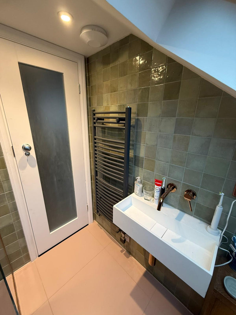 Compact luxury bathroom featuring green Zellige wall tiles, a wall-mounted floating sink, and bronze-finished modern faucets.