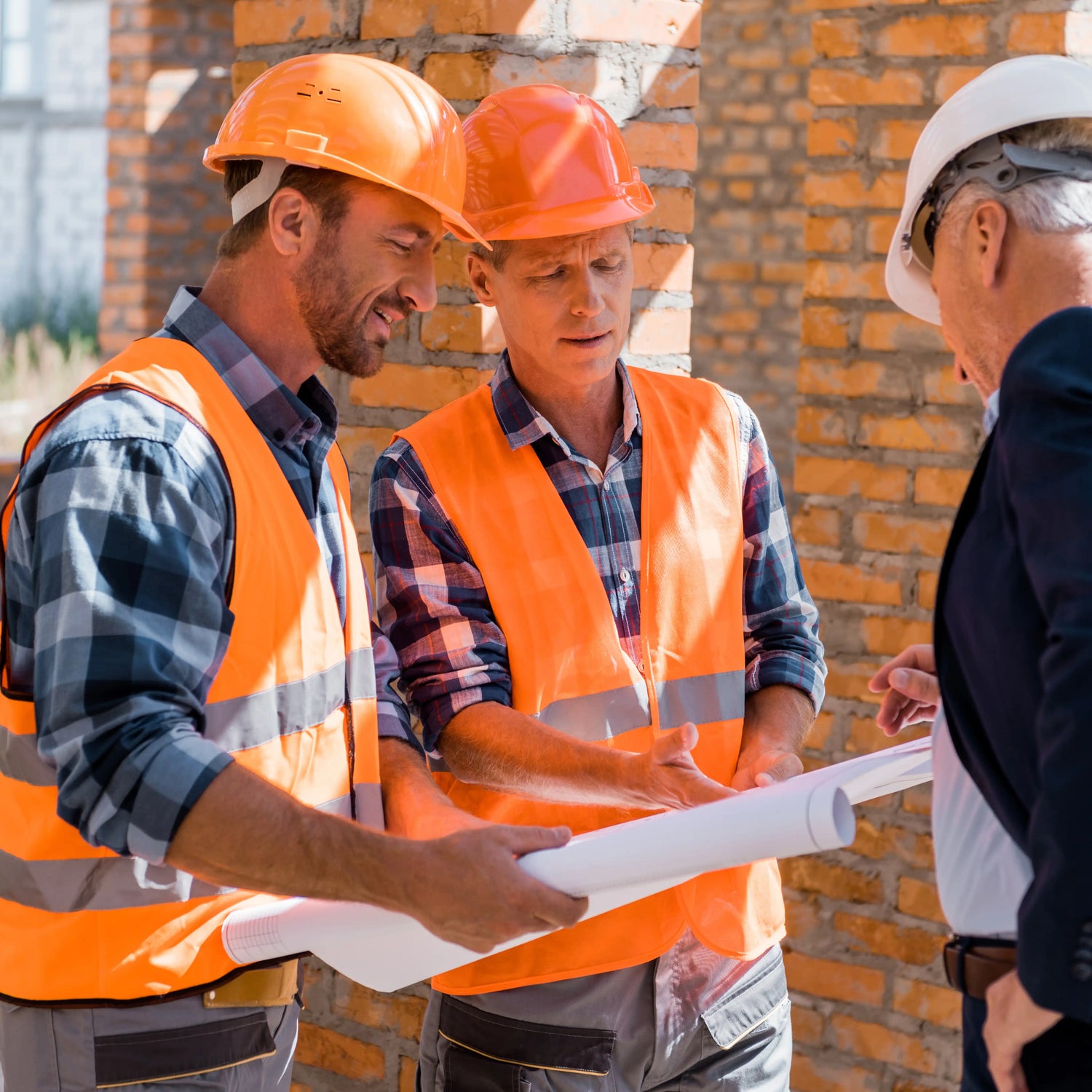 Brobrick Construction experts in orange safety vests and hard hats discussing building blueprints with a client on a London construction site.