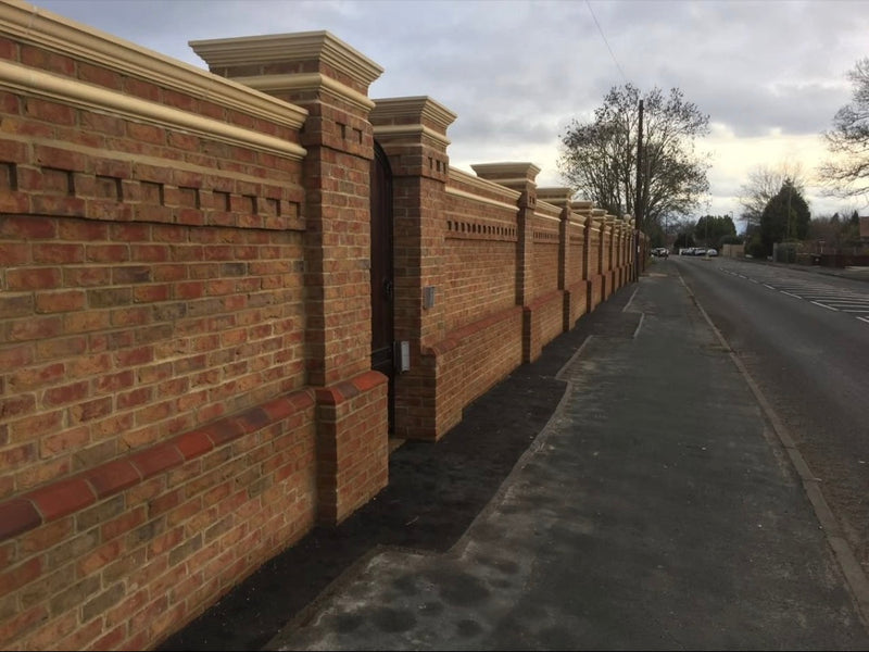 High-end decorative brick boundary wall featuring integrated pillars, dentil coursing, stone pier caps, and bullnose brick detailing.