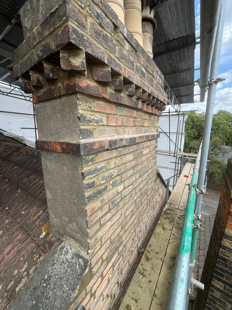 Close-up of a reconstructed chimney stack featuring decorative brick corbeling, traditional multi-stock bricks, and professional lime-style pointing on a period property.