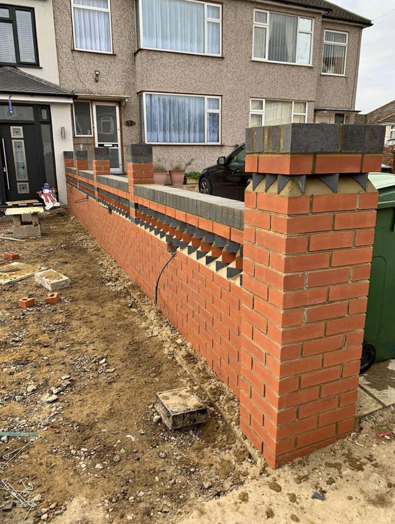 A bespoke front garden boundary wall featuring red facing bricks, blue engineering brick capping, and a decorative dogtooth brick pattern.