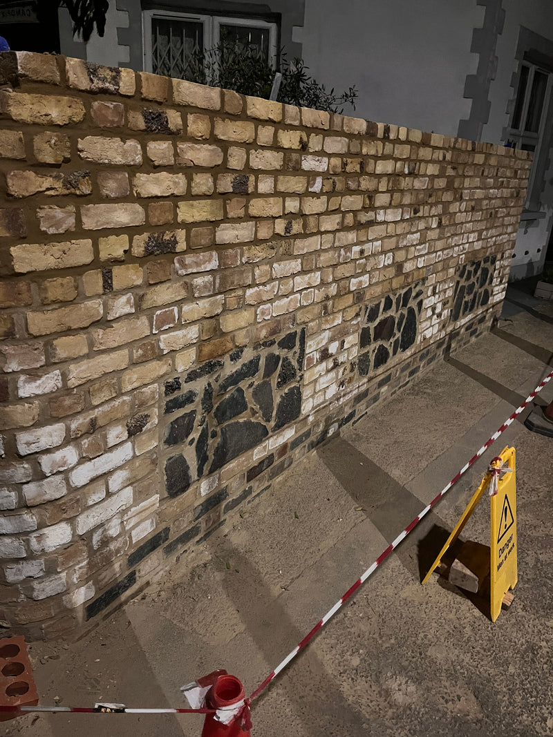 High-quality traditional masonry showing a flint and brick boundary wall under construction, highlighting expert heritage craftsmanship.