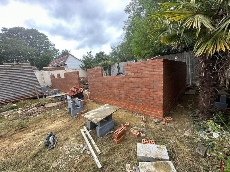A residential garden outbuilding under construction, featuring precision red facing brickwork and a structural engineering brick base on a London property.