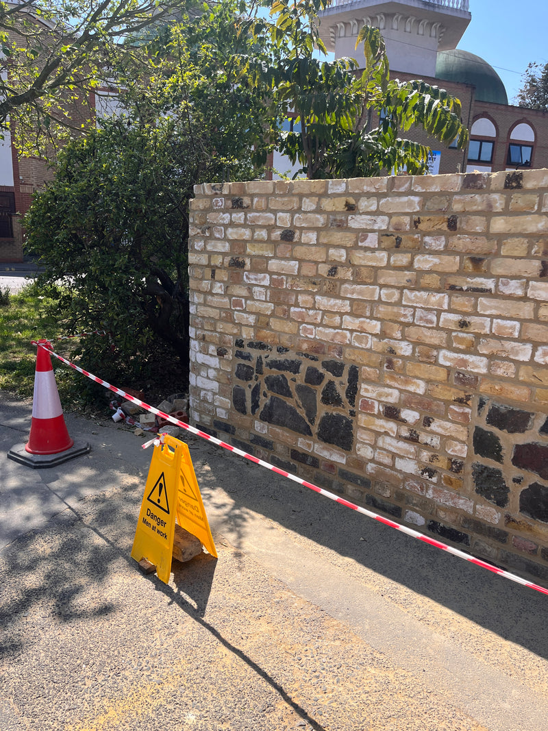 Daytime view of a traditional flint and brick boundary wall restoration, showcasing the combination of natural stone and reclaimed London stock bricks.