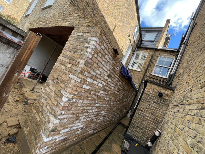 Side view of a completed house extension featuring yellow multi-stock brickwork, showing clean vertical alignment, a structural recessed opening, and seamless integration with the original building.