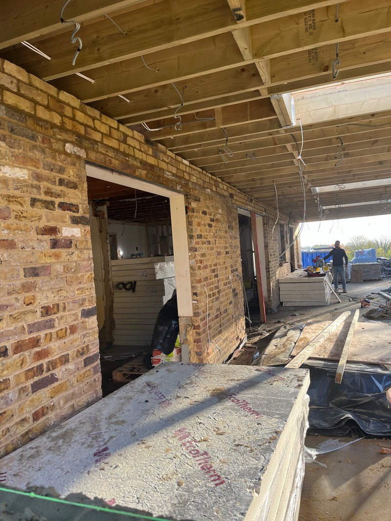 View of a residential extension project showing internal breeze block walls, a structural door opening with a concrete lintel, and the exterior red brick skin.