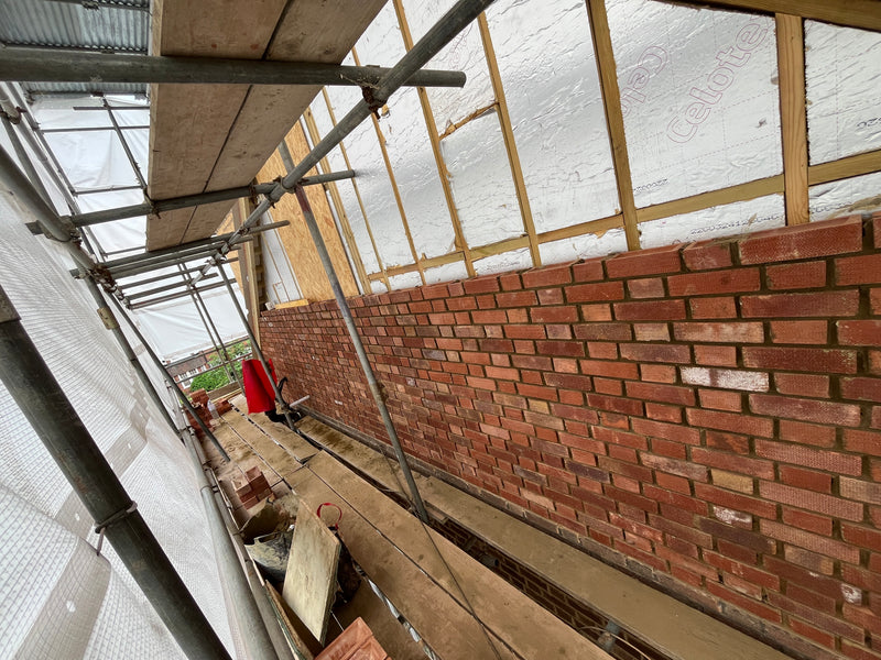 View from the scaffold showing red facing brickwork being integrated with high-performance Celotex cavity insulation and timber structural frames.