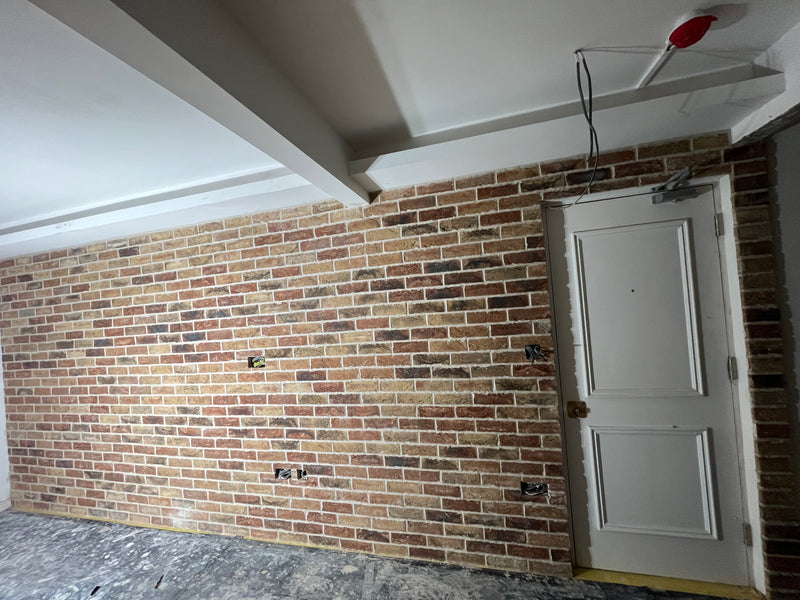 A completed internal feature wall made of multi-stock facing bricks, showcasing consistent mortar joints, a clean integration with a structural door frame, and precisely cutouts for electrical back-boxes.
