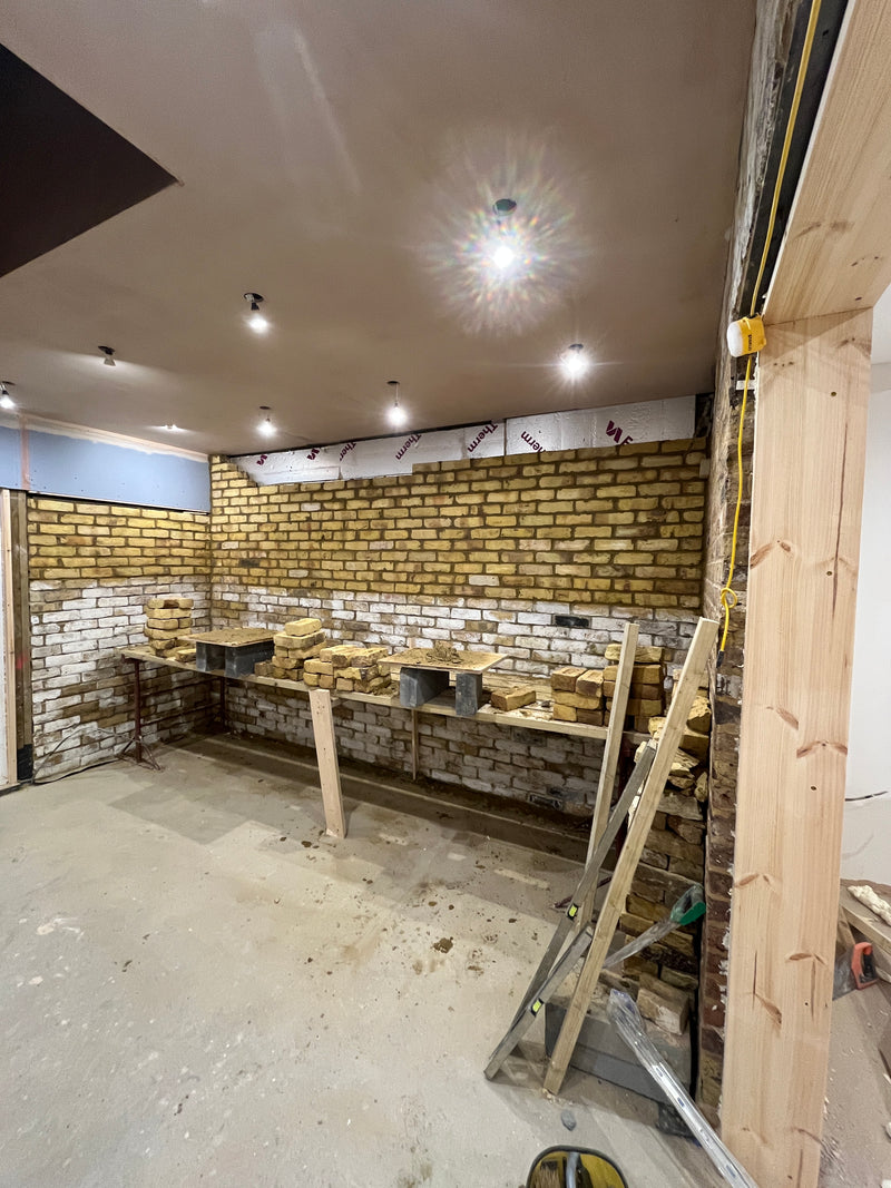 An internal exposed brick feature wall under construction in a London home, using traditional yellow stock bricks to create an industrial interior design aesthetic.