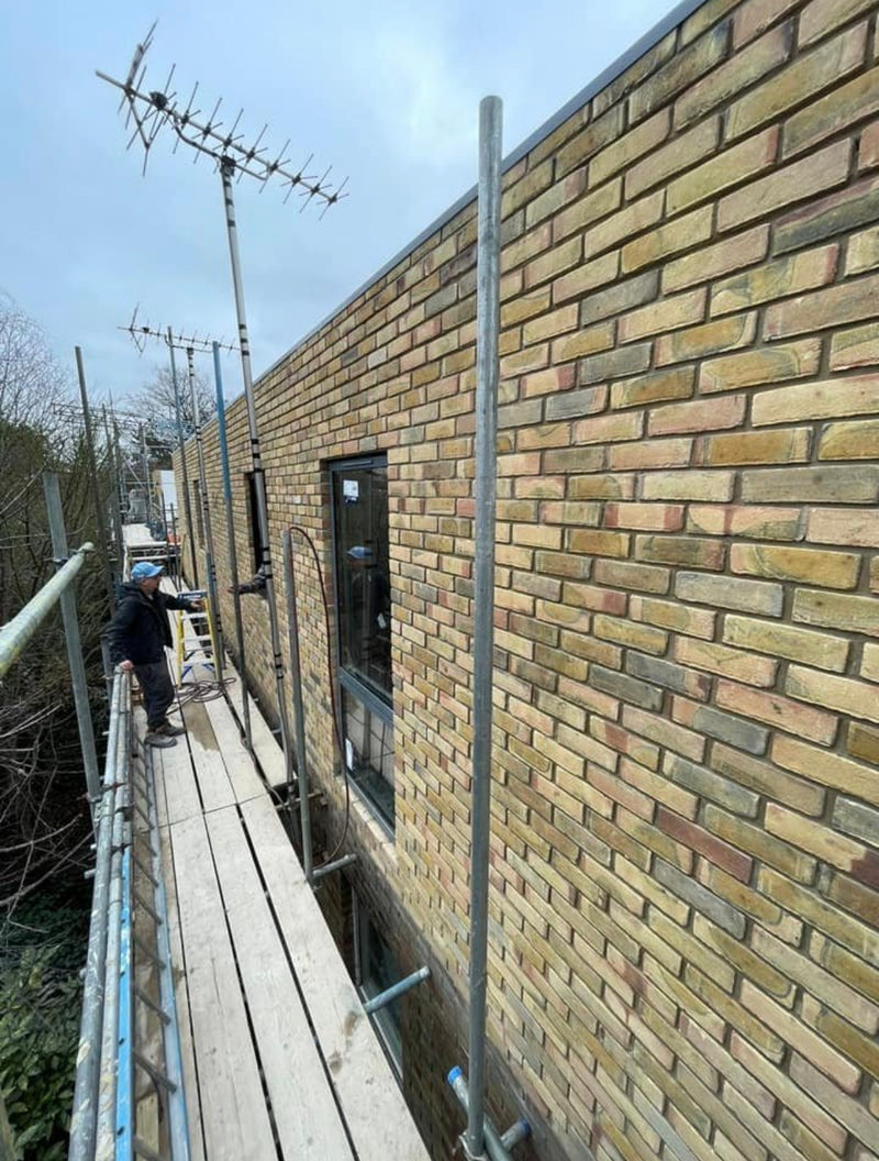 View from scaffolding of a completed large-scale yellow multi-brick elevation, showing consistent mortar joints and professional window integration.