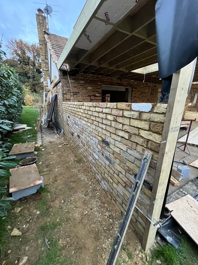 A wide-angle view of a significant house extension under construction, featuring multiple structural openings, red multi-stock brickwork, and internal breeze block walls.