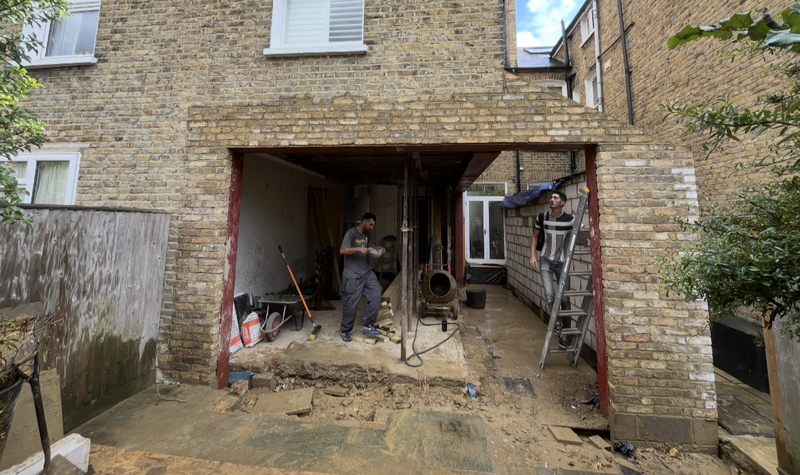 Contractors installing a wide-span structural steel frame for a rear house extension, replacing a load-bearing wall to create an open-plan living space.