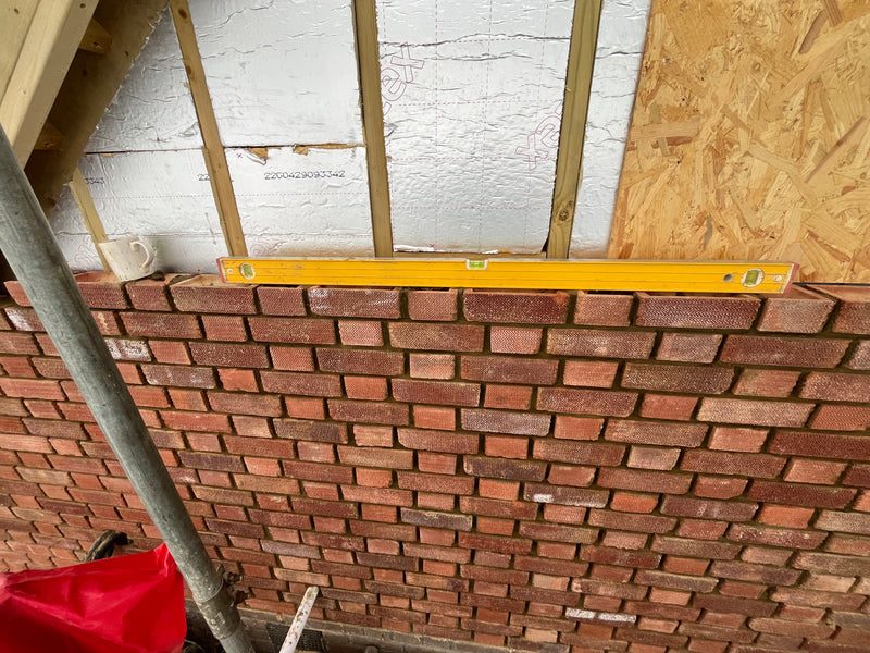 A spirit level resting on a newly laid course of red facing bricks, demonstrating perfectly horizontal alignment on a residential extension project.