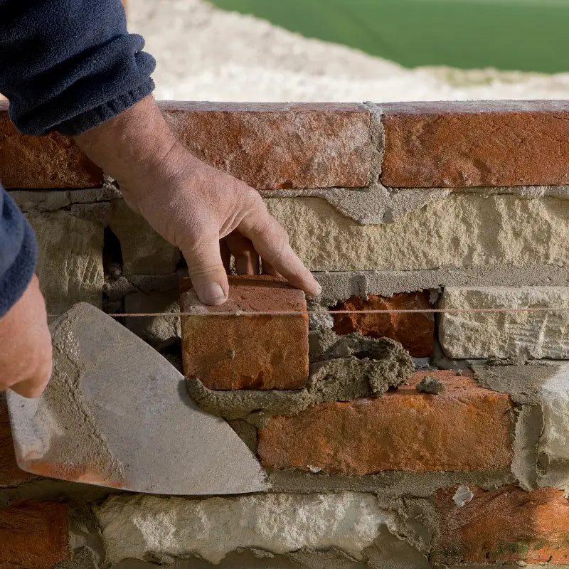 A professional London bricklayer carefully laying a red brick with mortar and a trowel to build a precise wall. (Brobrick Construction Ltd.)