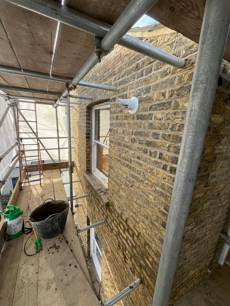 A professional London Stock brickwork restoration on a scaffolded site, showing expert repointing, a clean finish around sash windows, and integrated external ventilation.