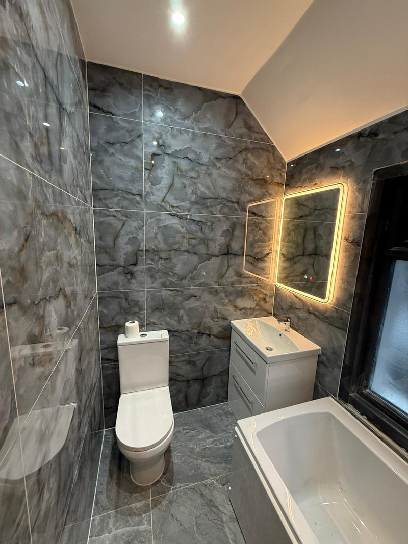 A high-end bathroom renovation featuring marble-effect large format porcelain tiles, a modern white vanity unit, and a backlit LED mirror in a bespoke London home.