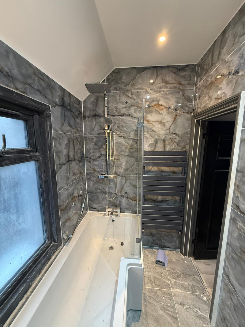 A high-end bathroom renovation featuring floor-to-ceiling blue marble-effect porcelain tiles, an L-shaped shower bath with a glass screen, and a dark grey heated towel rail.