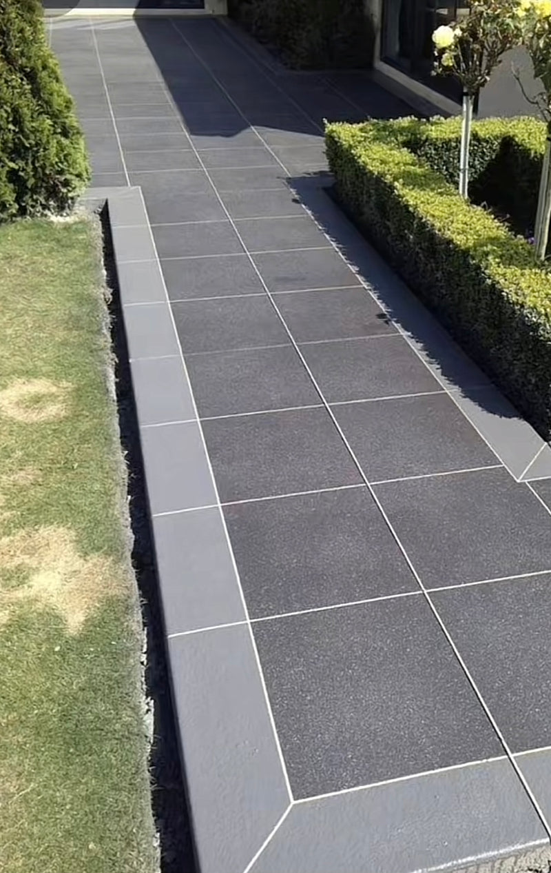 A contemporary garden walkway featuring dark grey anthracite porcelain tiles with a matching mitered border and professional landscaping in a London residential garden.