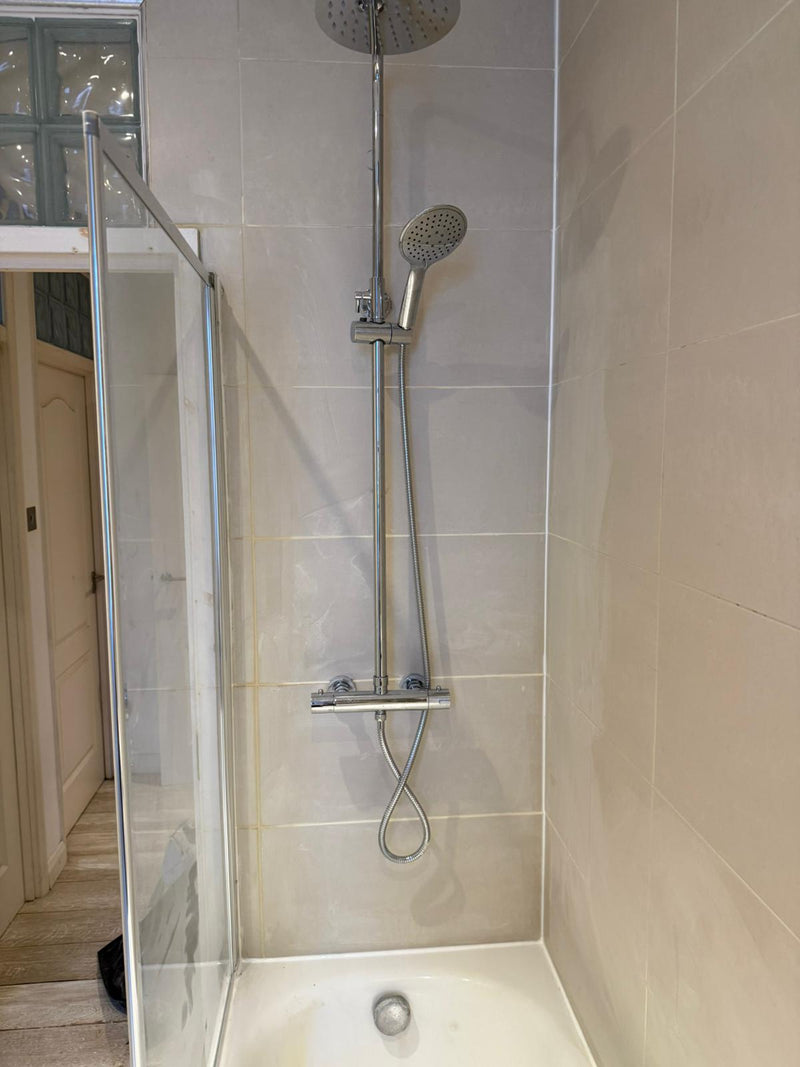 Professional bathroom tiling featuring large-format porcelain wall tiles and a luxury chrome rainfall shower installation in a London home renovation.