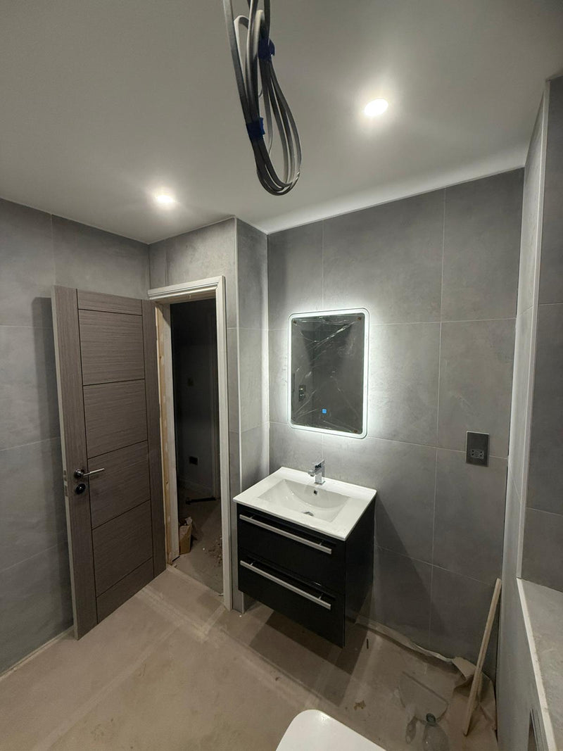 A contemporary bathroom featuring a floating black vanity unit, an illuminated LED mirror, large-format grey wall tiles, and a modern grey internal door.