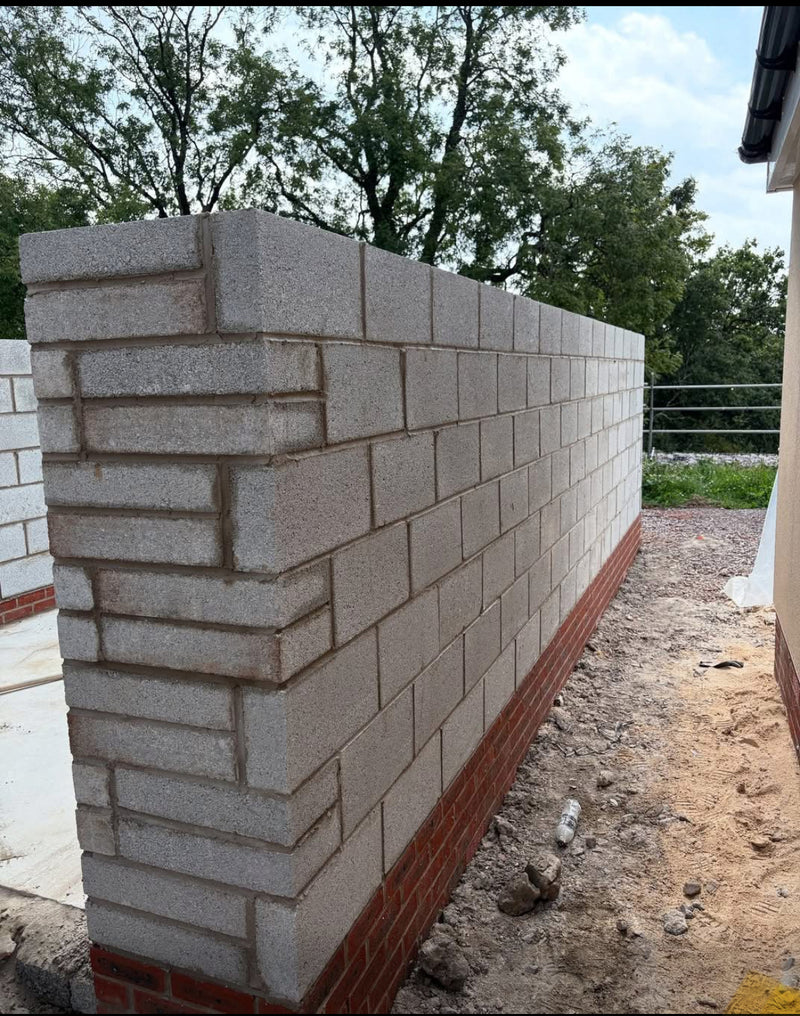 Perspective view of a long structural blockwork wall with red brick base courses, demonstrating perfect horizontal alignment and clean mortar joints.