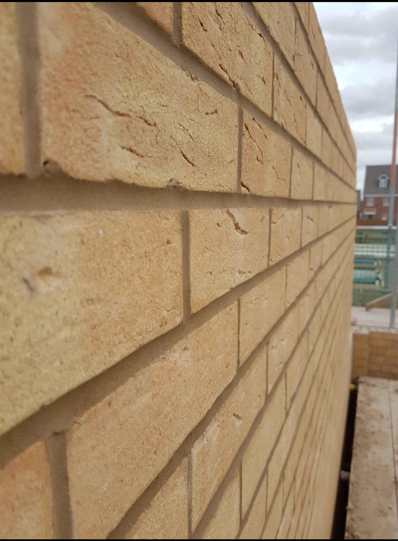A close-up perspective of a newly constructed external wall using buff-colored facing bricks with clean, uniform mortar joints and perfect alignment.
