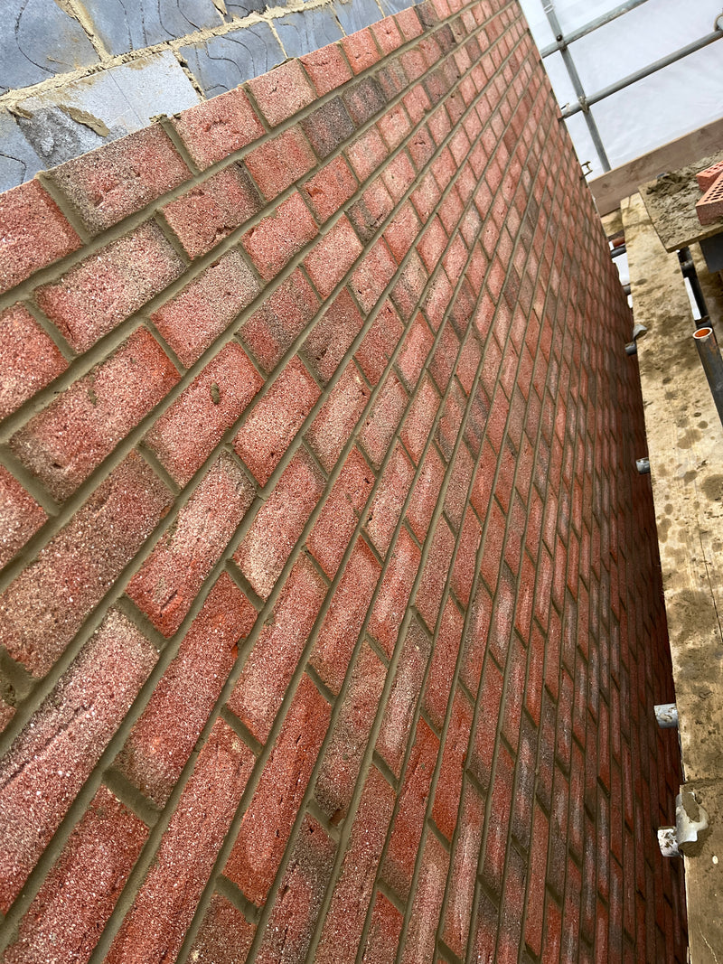 A close-up of high-quality red facing bricks stacked on a pallet alongside fresh wet mortar on a construction site. This highlights the premium materials Brobrick Construction uses for all London masonry and brickwork projects.