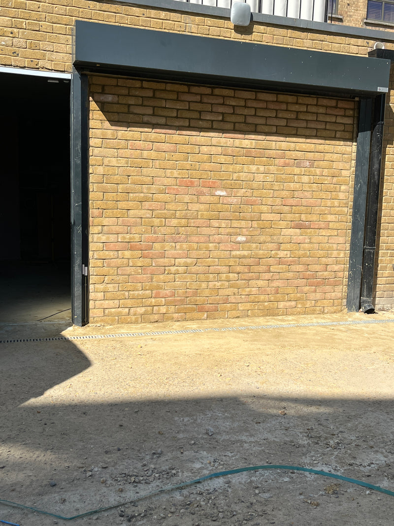External view of a private parking garage featuring professional buff brick masonry, integrated roller shutter tracks, and a clean threshold drainage system.
