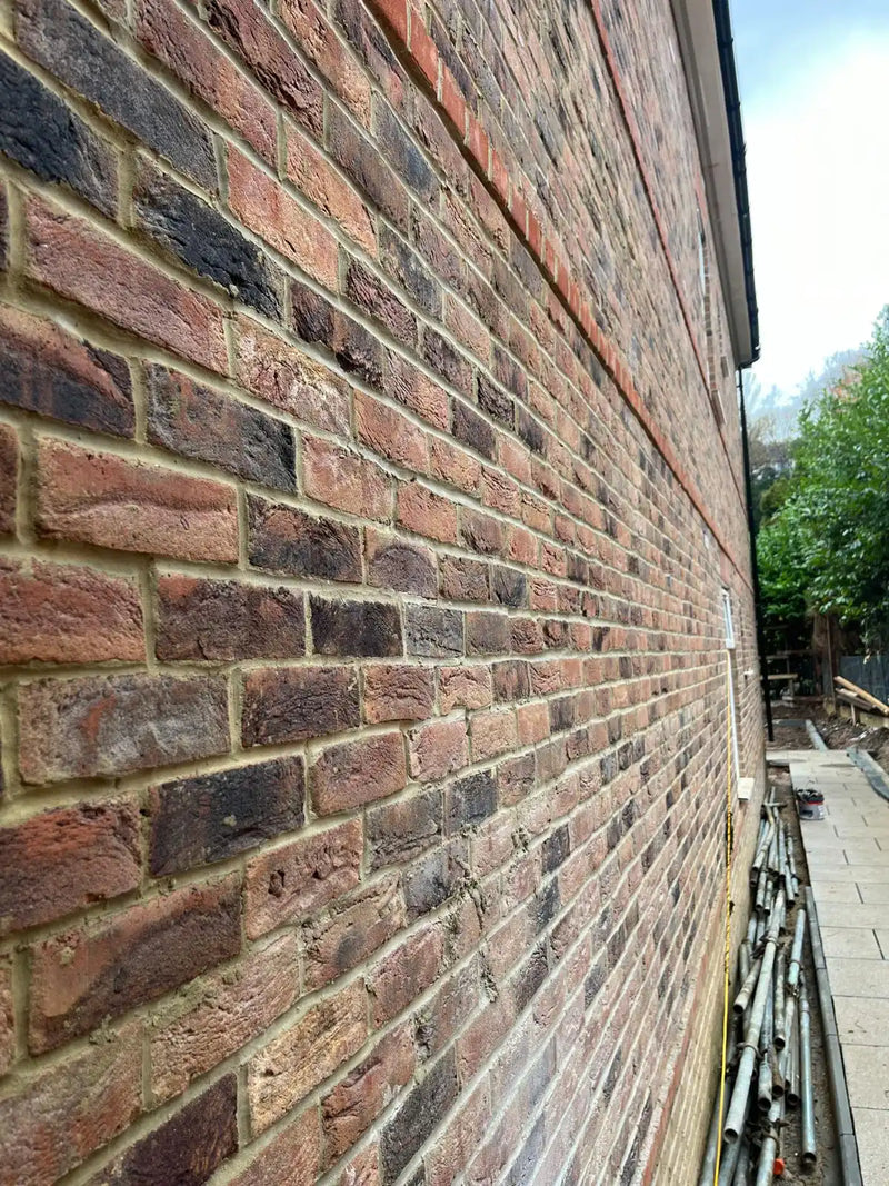 A perspective view looking down a long, expertly crafted red and charcoal multi-tone brick wall. The image showcases clean mortar joints, precise brick alignment, and a decorative soldier course of bricks, demonstrating high-quality residential masonry in London.