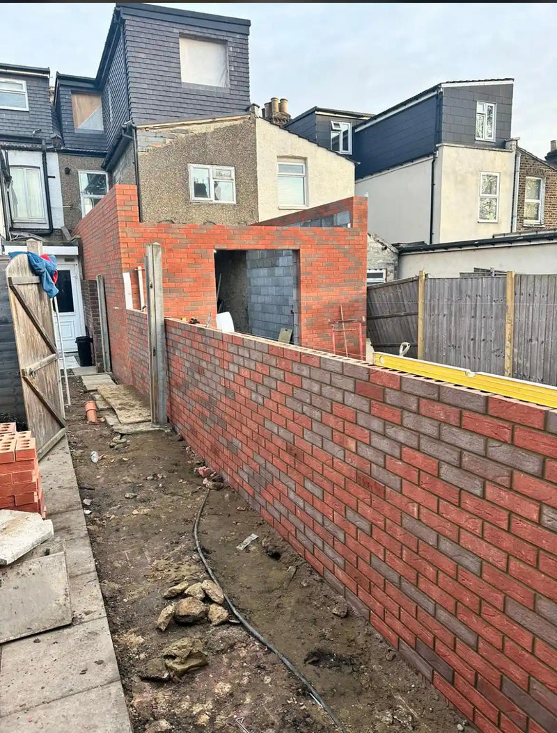 A rear house extension in London showing the new brickwork shell and a long boundary wall. The photo highlights clean mortar lines, a professional spirit level resting on the wall, and the structural progress of a modern residential home expansion.