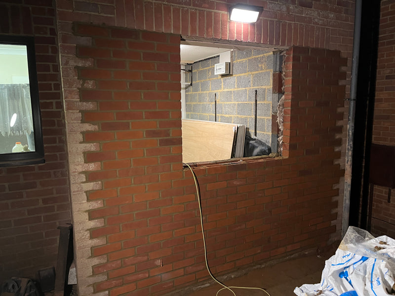 Close-up of a structural masonry repair showing new red bricks being toothed-in to an existing wall, with a clear view of the internal blockwork leaf and cavity.