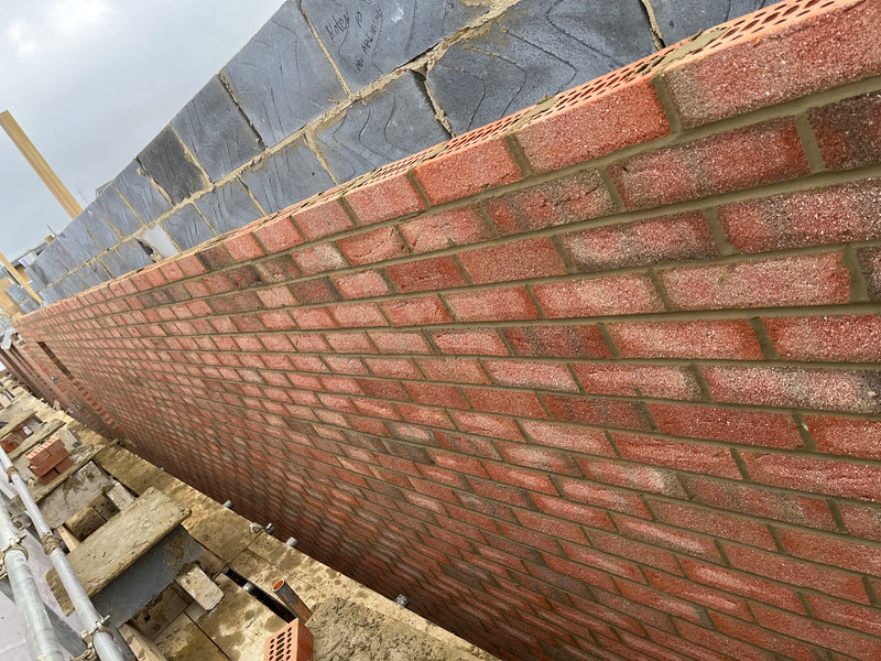 A residential construction site in London featuring a long brick wall under development. The scene shows stacks of red facing bricks, fresh mortar, and a professional bricklayer’s setup, highlighting Brobrick Construction’s capacity for large-scale masonry projects.