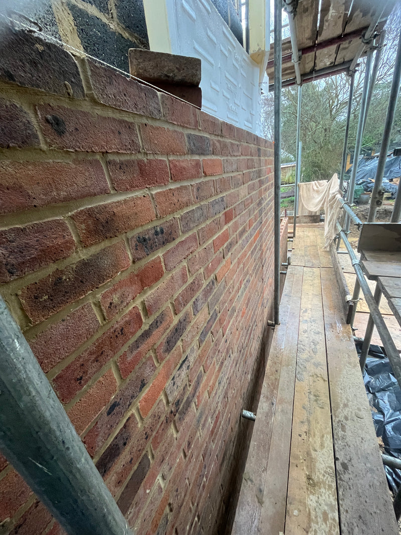 Close-up of high-quality red brickwork on a residential house extension, showing clean mortar joints and professional scaffolding on a London site.
