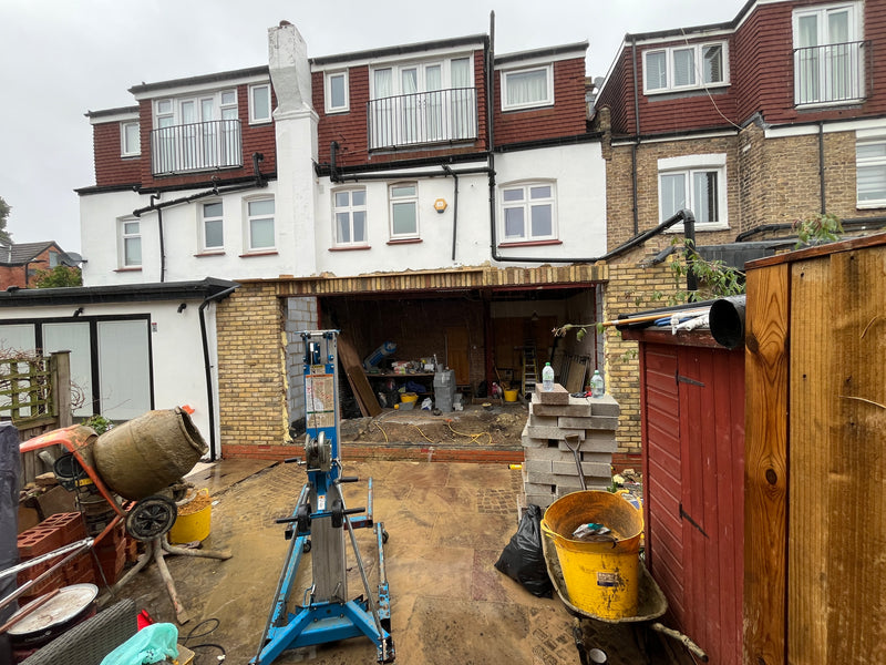 Site view of a rear house extension featuring a Genie lift for structural steel RSJ installation, cement mixer, and blockwork staging.