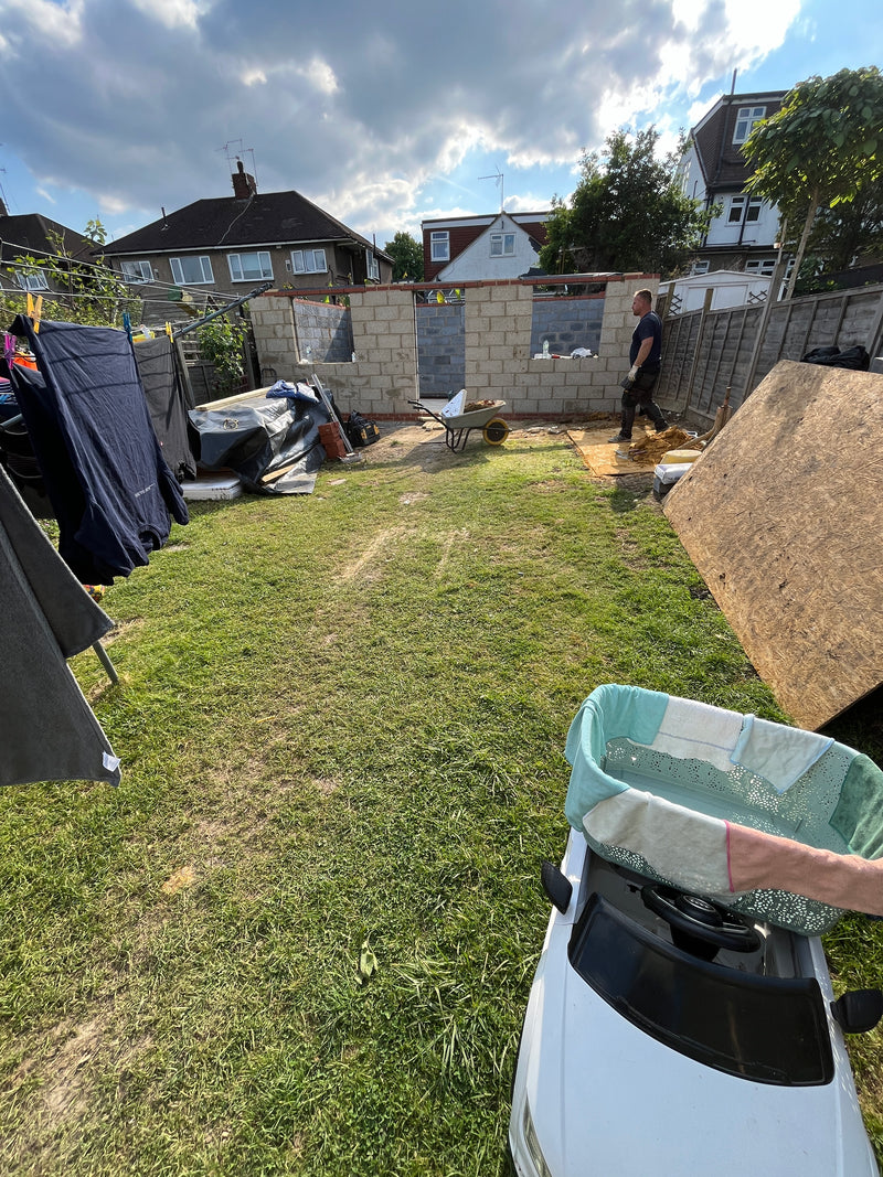A wide view of a residential garden construction site in London, showing the structural blockwork shell for a new outbuilding or home office.