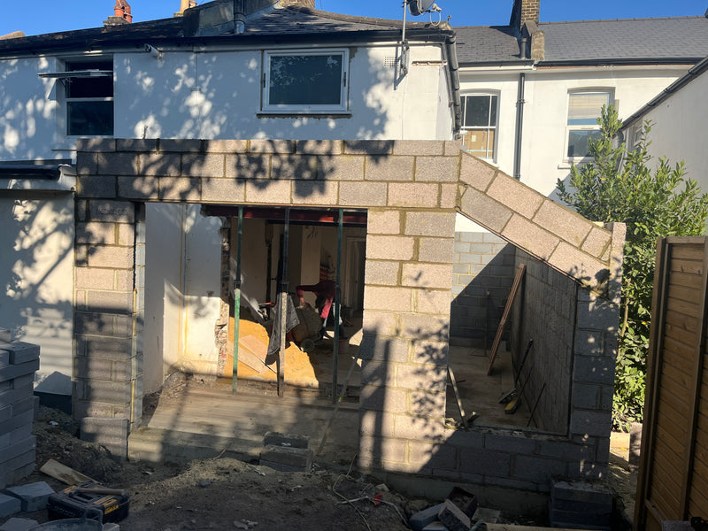 View of a rear house extension internal blockwork shell, showing wide-span structural openings and a sloped masonry gable end.