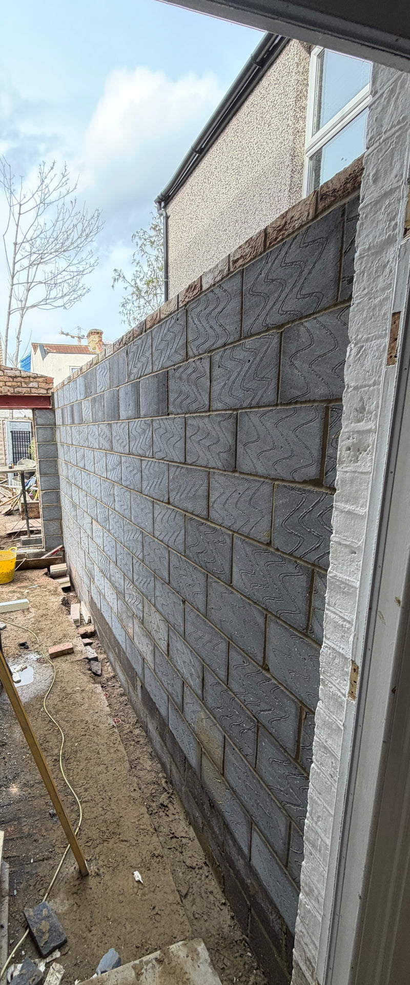 A wide-angle interior view of a new-build structural blockwork extension. The image shows the completed inner leaf of a large masonry wall using high-quality serpentine-textured blocks, providing a mechanical key for future plastering. The perspective highlights perfect vertical and horizontal alignment, a clean construction site, and a large structural opening supported by steel at the far end.