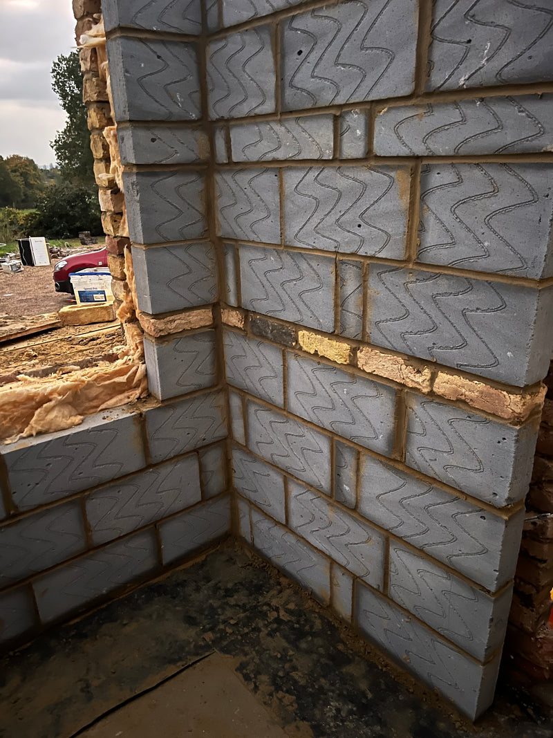 A technical close-up of structural breeze block masonry for a residential extension, showing professional corner bonding and thermal insulation cavity ties.