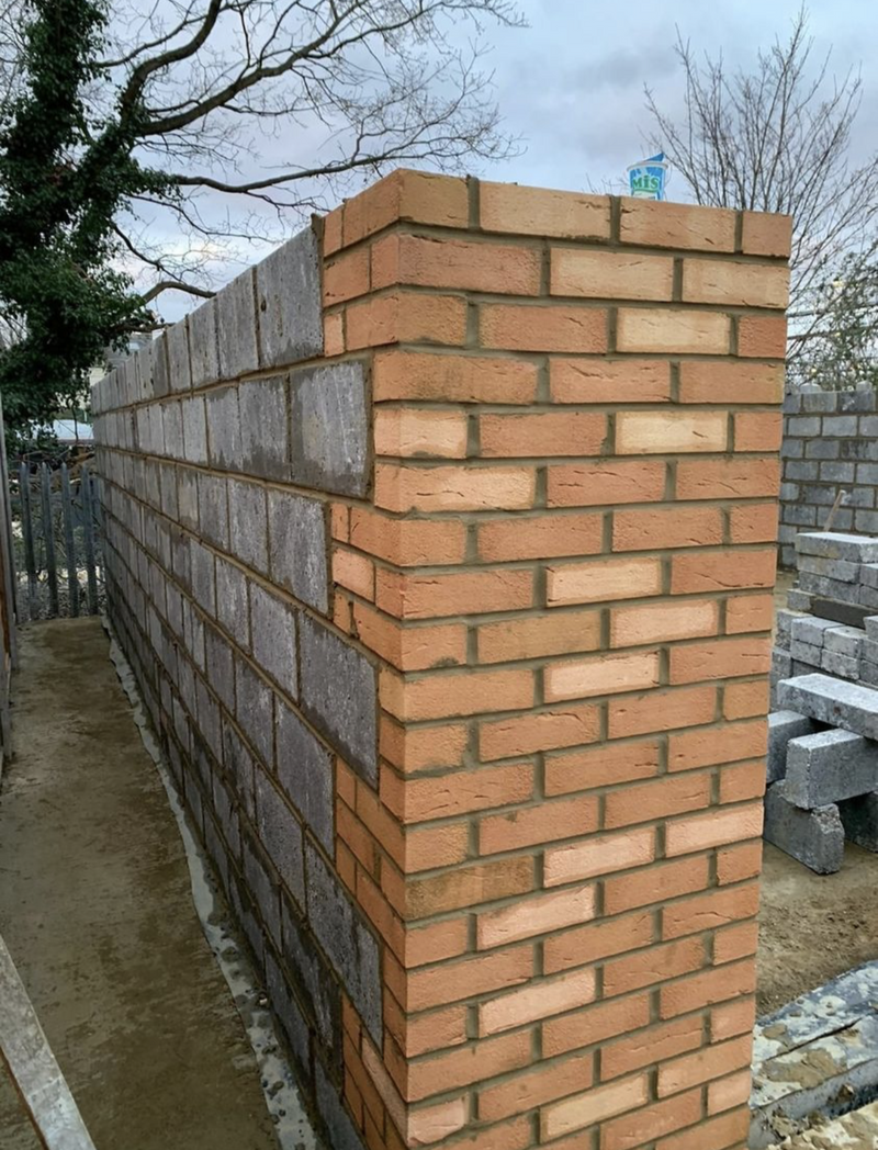A detailed view of a structural corner featuring perfect brick bonding with external red bricks and internal grey breeze blocks for a durable house extension.