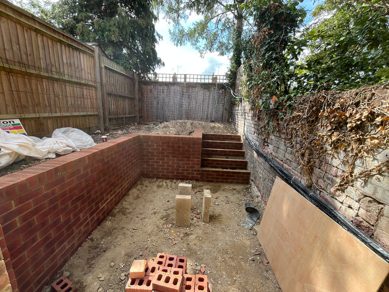 Construction of a multi-level red brick retaining wall and integrated garden steps, showing professional bonding and earth-retention engineering.
