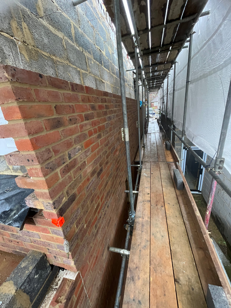 Side profile of a house extension under construction, showing the integration of red facing bricks and internal thermal breeze blocks from a professional scaffold.