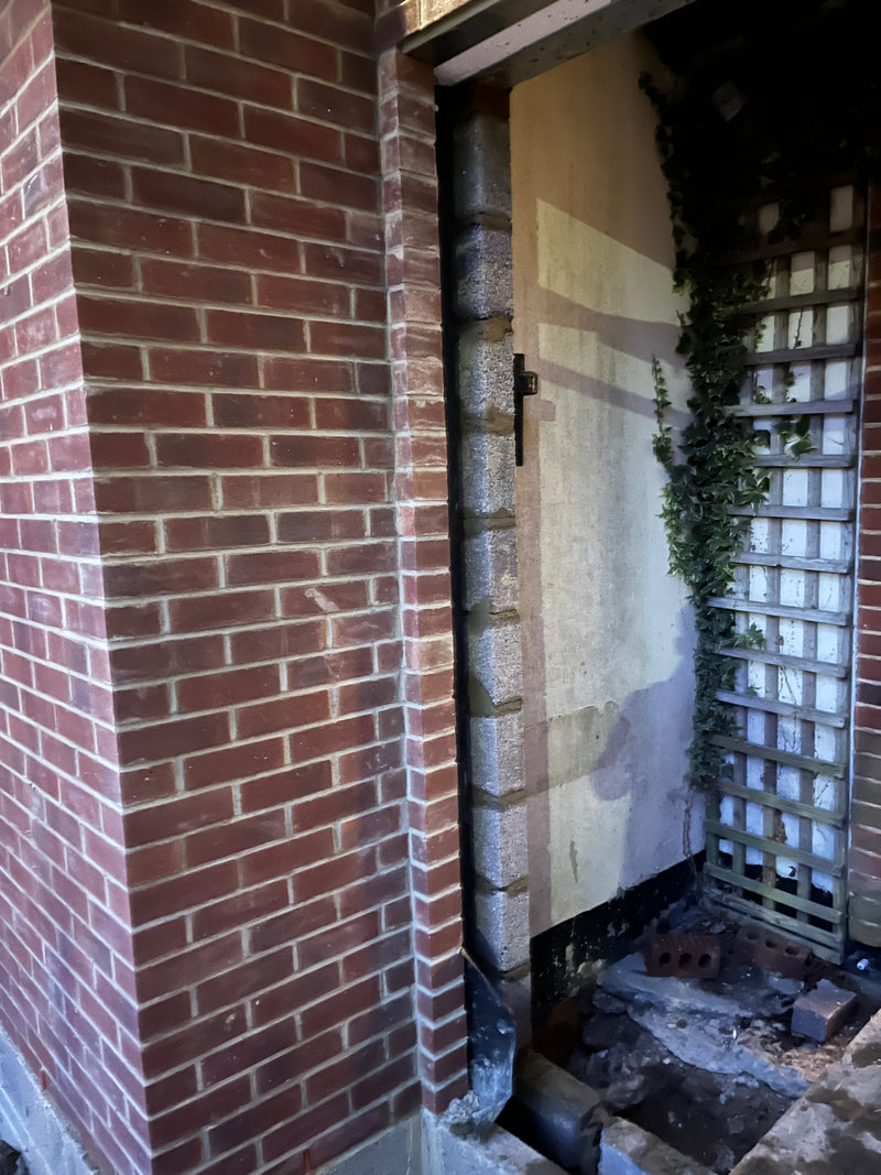 Close-up of a new red brick pillar and internal blockwork column integrated with an existing property wall, showing a structural steel lintel and precise vertical bonding.