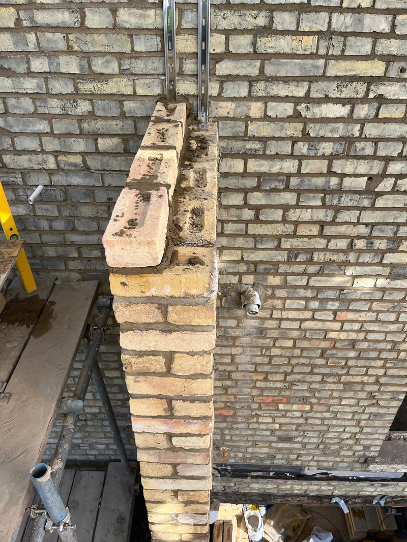 Top-down view of a structural brick pier being tied into an existing wall using stainless steel starter tracks and lateral wall ties for maximum stability.
