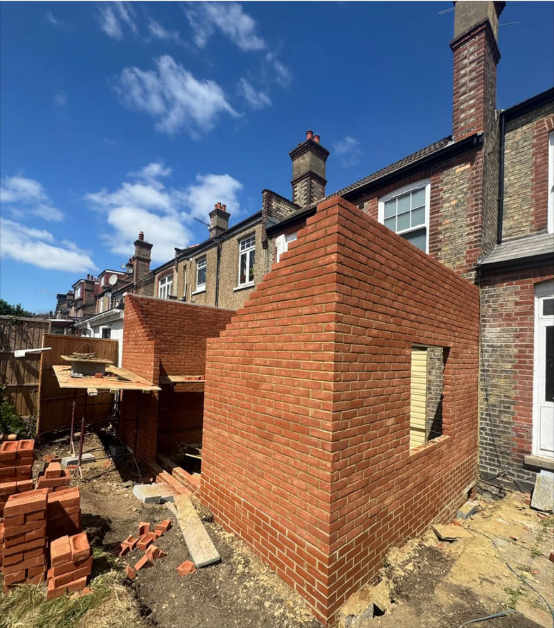A rear house extension under construction featuring red multi-stock brickwork, showing clean gable ends and precise corner bonding in a residential setting.