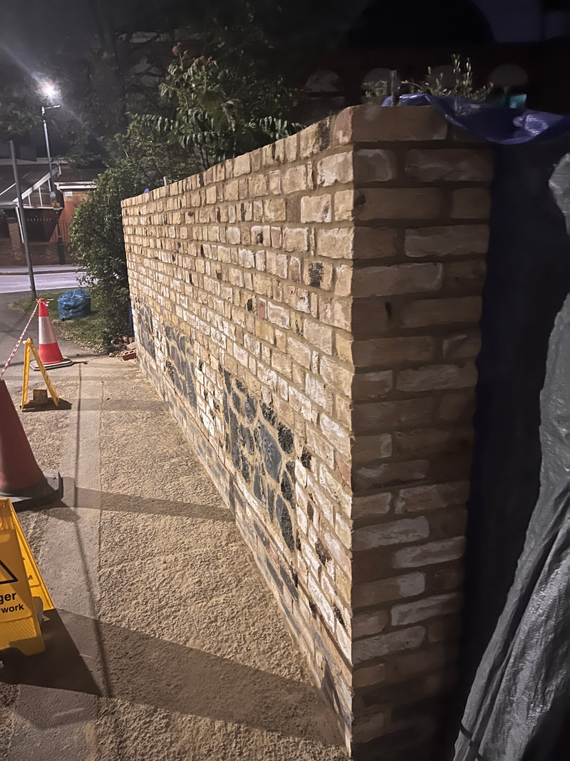 A tall, professionally constructed boundary wall featuring a decorative flint stone base and a traditional London stock brick upper section.