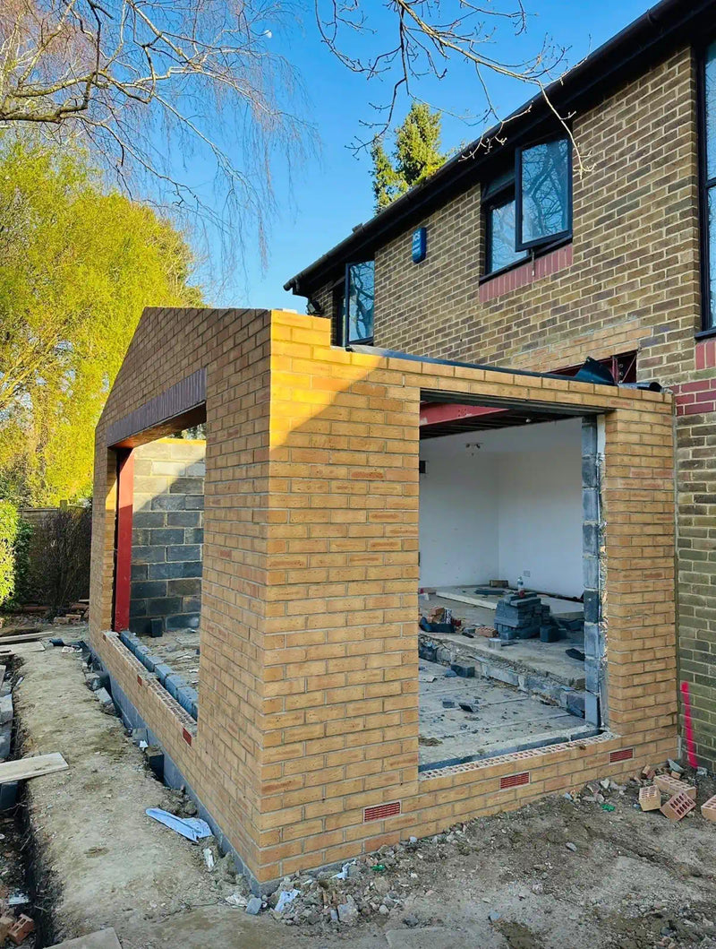 Front elevation of a yellow multi-stock brick rear house extension in London showing the full-width bifold door opening, structural steel lintel with red brick course, and the existing property above. Built by Brobrick Construction Ltd.