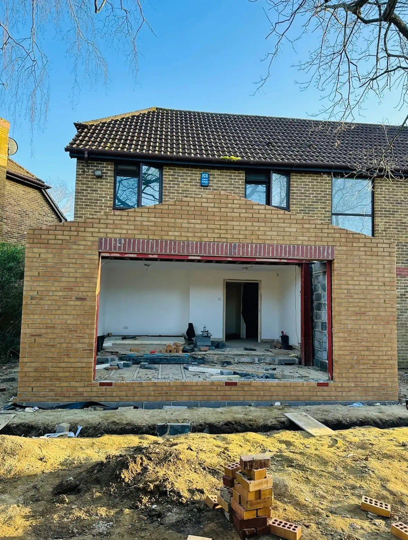 Yellow multi-stock brick rear house extension under construction in London, showing the brickwork shell, large structural opening with steel lintel, and drainage channel at the base. Built by Brobrick Construction Ltd.